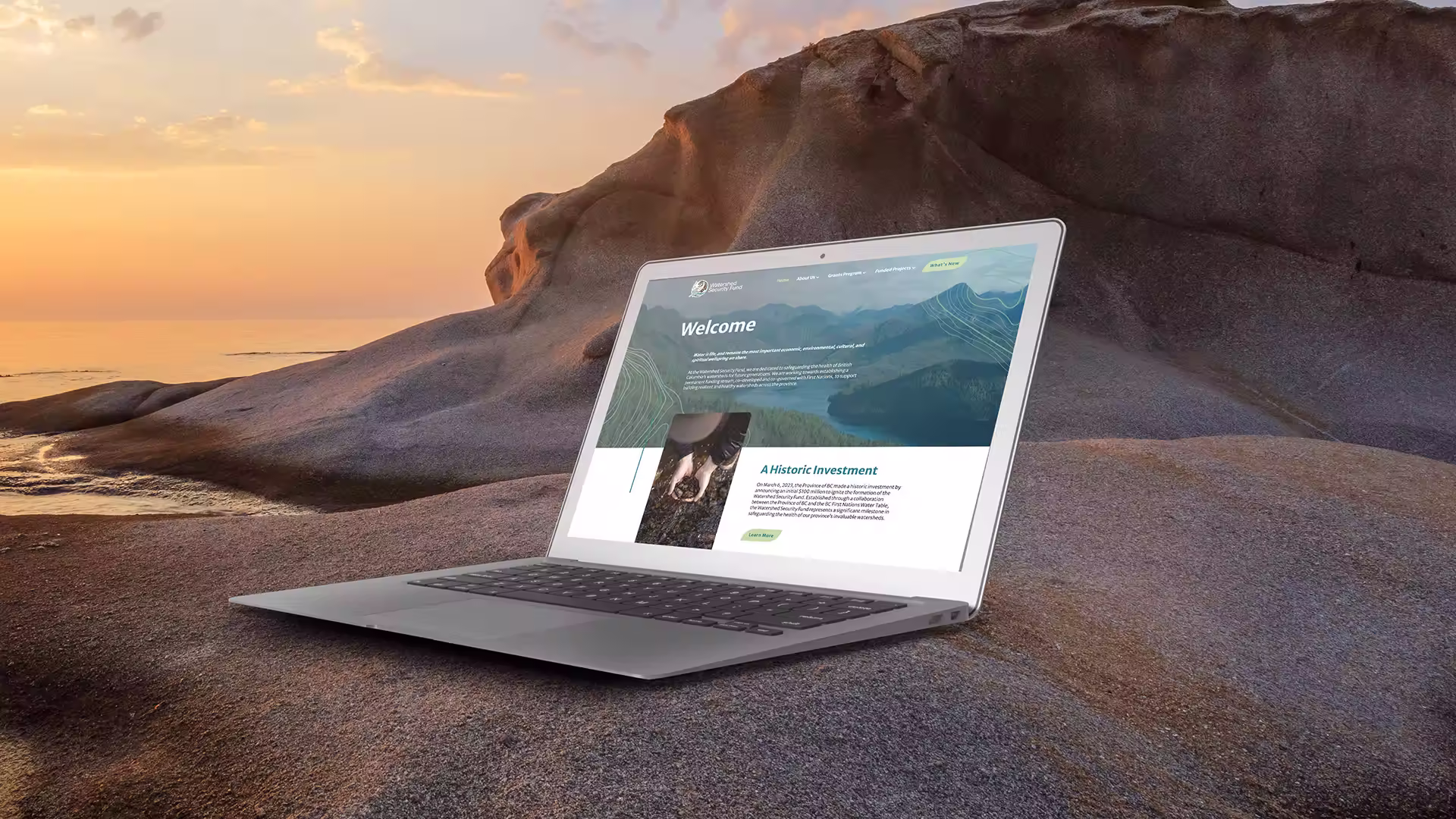 Laptop displaying a website about a historic investment on a rocky beach at sunset.